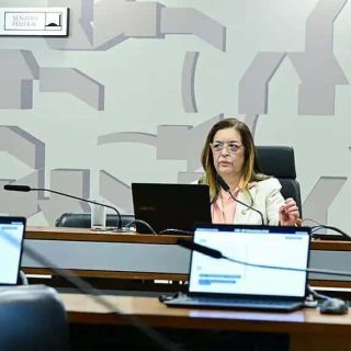 Legislação e debates no Congresso Nacional sobre justiça, direito e assuntos sociais no Brasil. Imagem de uma mulher participando de reunião no plenário, com computadores e painel ao fundo.