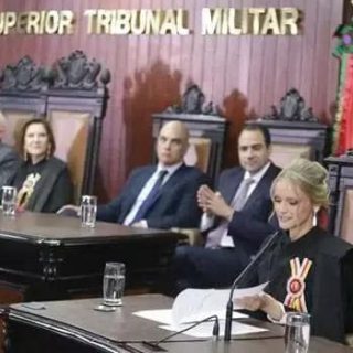 Julgamento no Superior Tribunal Militar com ministros e advogada apresentando defesa, em ambiente formal com decoração de madeira e escudos do tribunal.