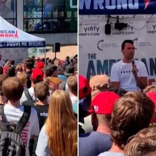 Ativistas protestando em evento político com grande público em frente ao palco ao ar livre.