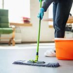 Limpeza doméstica profissional sendo realizada com esfregão e balde de água em ambiente de escritório.