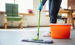Limpeza doméstica profissional sendo realizada com esfregão e balde de água em ambiente de escritório.