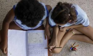 Crianças estudando juntos no chão com caderno e canetas, promovendo educação e inclusão social.