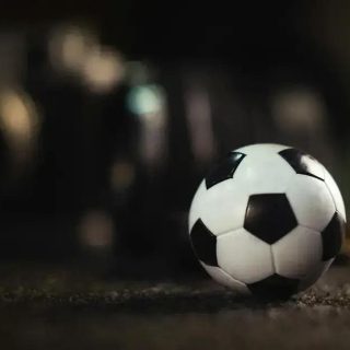 Bola de futebol em destaque na imagem, com fundo escuro e iluminação suave, representando esportes e jogos.