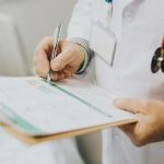 Exame médico em ambiente hospitalar com profissional anotando resultados em prontuário médico.