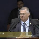 Advogado em tribunal durante sessão de julgamento de caso de direito, com outros profissionais ao fundo.