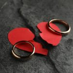 Quebra de relacionamento com alianças de casamento e papel rasgado vermelho, símbolo de divórcio ou separação, em fundo de pedra escura.