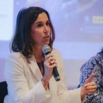 Advogada falando em evento jurídico com microfone, ambiente profissional, woman com expressão séria, discutindo temas de direito, destaque em notícias jurídicas, evento de direito hoje.