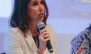 Advogada falando em evento jurídico com microfone, ambiente profissional, woman com expressão séria, discutindo temas de direito, destaque em notícias jurídicas, evento de direito hoje.