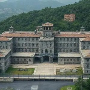 Castelo histórico no centro de uma cidade com montanhas ao fundo, destacando-se por sua arquitetura antiga e importância cultural no contexto do direito e história.