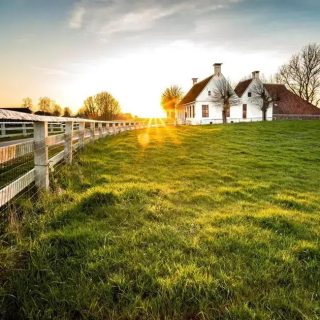 Fazenda rural com casa branca ao pôr do sol, cercada por árvores e gramado verde, ambiente tranquilo e ideal para viver em contato com a natureza.
