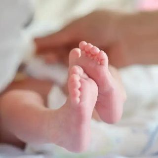 Recém-nascido nos braços da mãe com foco em seus pequeninos pés.