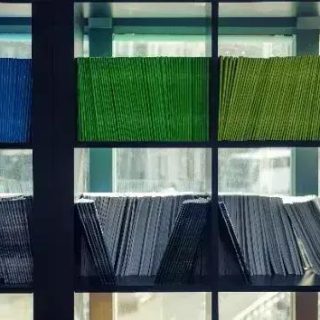 Arquivos de documentos organizados em estantes de escritório, de diversas cores.