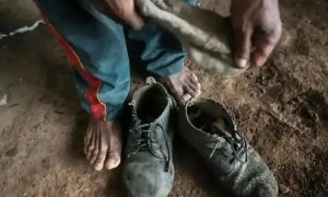 Sapatos velhos e usados em solo de terra, mãos sujas de terra e pés descalços, evidenciando trabalho rude ou situação de vulnerabilidade social, tema relevante para notícias de direitos e justiça.
