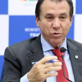 Advogado falando em evento do Ministério do Trabalho com fundo azul e logos do MTE.