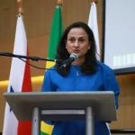 Usuária fala na tribuna durante evento de Direito Hoje Notícias, com bandeiras do Brasil, Estados Unidos e Brasil ao fundo, reforçando temas de direito e justiça.
