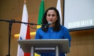 Usuária fala na tribuna durante evento de Direito Hoje Notícias, com bandeiras do Brasil, Estados Unidos e Brasil ao fundo, reforçando temas de direito e justiça.