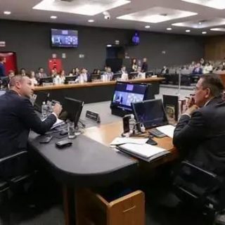 Audiência judicial com advogados e profissionais do direito em ampla sala de tribunal, com computadores e documentos discutindo casos legais e legislativos.