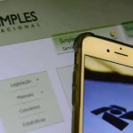 Simpes Nacional logo e smartphone mostrando acesso digital a serviços jurídicos e notícias atuais.