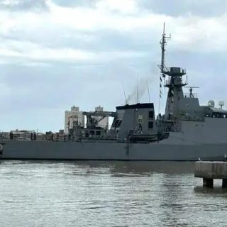 Navio de guerra militar navegando próximo à cidade, com céu nublado ao fundo, símbolo de defesa e segurança marítima, destaque em notícias de direito e força naval.