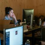 Operadora de atendimento ao cliente usando headset em ambiente de escritório com computadores e informações jurídicas, representando direitos e notícias jurídicas atuais.