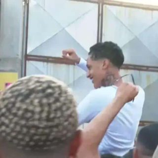 Homem celebrando vitória com alegria e apoio de pessoas ao redor, em ambiente de evento ou reunião social.