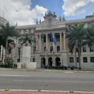 Faculdade de Direito vista frontal com árvores e bandeiras na frente, imagem de uma instituição de ensino superior com foco em notícias e informações jurídicas.