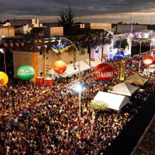 Multidão e festividades ao ar livre em evento com iluminação e balões coloridos, promovendo cultura e diversão na cidade. Evento popular com grande presença de público, música e shows em espaço urbano.