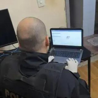 Policial da Polícia Federal usando laptop para investigação digital em ambiente interno, concentrado na análise de dados.