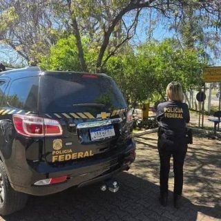 Polícia Federal em ação de fiscalização com carro oficial na rua, polícia feminina de costas observando a operação na área urbana sob céu claro, destaque em segurança e investigação policial.