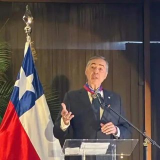 Brasileiro em discurso político ao lado das bandeiras do Brasil e Grécia, destacando temas de direito e política internacional, com foco em notícias e atualidades do Direito Hoje Notícias.