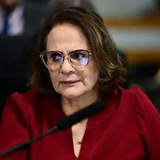 Associação de mulheres advogadas, mulher com óculos, expressão séria, em ambiente de tribunal ou reunião jurídica.