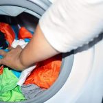 Lavanderia de roupas em uma máquina de lavar roupa com roupas coloridas e uma pessoa colocando roupas na máquina.