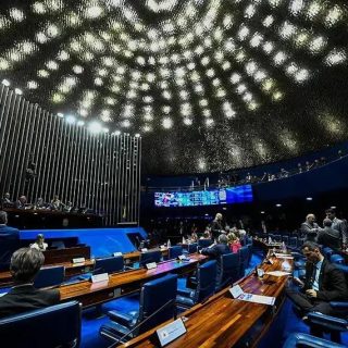 Político discutindo em plenário de congresso nacional em ambiente moderno e formal, com destaque para a cúpula de teto iluminada e tecnologia avançada, representando temas de Direito, política e leis.