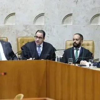Julgamento no tribunal com juízes e advogados no plenário, incluindo uma mulher idosa, em sessão relacionada ao direito e às notícias atuais do setor jurídico.