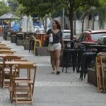Mesma, limpos e vazios, mesas de restaurante ao ar livre na calçada de uma rua movimentada com veículos estacionados ao fundo, durante o dia.