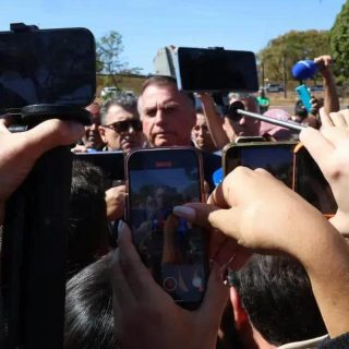 FOTO DE UMA ENTREVISTA OU EVENTO POLÍTICO, COM PESSOAS USANDO CELULARES E GRAVANDO, CENTRO DE ATENÇÃO PARA JORNALISTAS E REPÓRTERES.