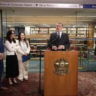 Deputado em pronunciamento na biblioteca do congresso com grupo de colegas ao fundo, ambiente formal com livro e gravatas, destaque nas notícias de direito hoje, evento político ou jurídico relevante.