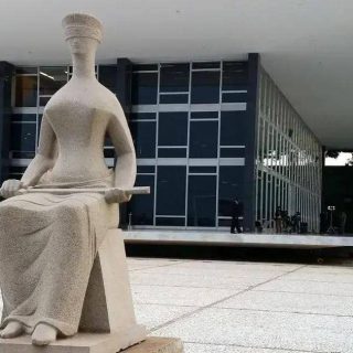 Estátua de mulher com toga e livro na frente do prédio do Supremo Tribunal Federal em Brasília, símbolo do poder judiciário e da justiça no Brasil, representando a importância do direito e do estado de direito.