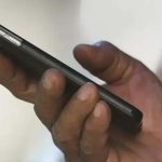 Celular smartphone preto sendo segurado por mão de pessoa, foco no aparelho, tecnologia, comunicação, direito hoje notícias.