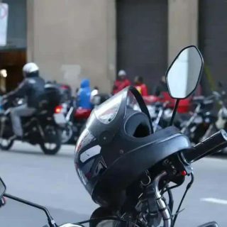 Capacete de moto estacionado na rua com vários motociclistas ao fundo, em ambiente urbano, destacando segurança no trânsito para artigos de direito e leis de trânsito.