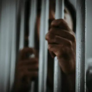 Prisão com grades de metal e mão visível em uma cela, simbolizando temas de direito penal e justiça.
