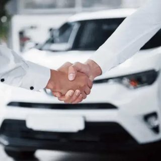 Acordo de handshake entre vendedores de carros no showroom, simbolizando negócio fechado e confiança na negociação.