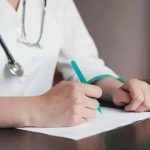 Exame médico sendo realizado por profissional de saúde usando jaleco branco e estetoscópio.