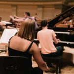 Artesãos de música clássica em ensaio orquestral com piano, violino e outros instrumentos, jovens músicos praticando em ambiente de estúdio musical.