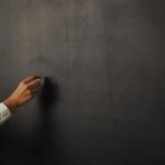 Fachada de quadro-negro com mão escrevendo com giz, símbolo de educação, escola ou aula, conceito de aprendizado e ensino, ambiente escolar, educação formal, sala de aula moderna, imagem representativa de ensino e formação profissional.