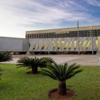 Edifício do Congresso Nacional em Brasília, sede do poder legislativo no Brasil, com jardim bem cuidado na frente e céu claro ao fundo.
